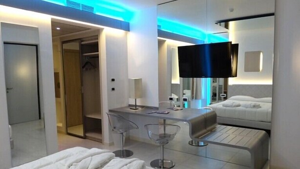 A modern hotel room with a bed, a desk, a chair, a TV, and a mirror. - Hotel Camelia (Cameri)