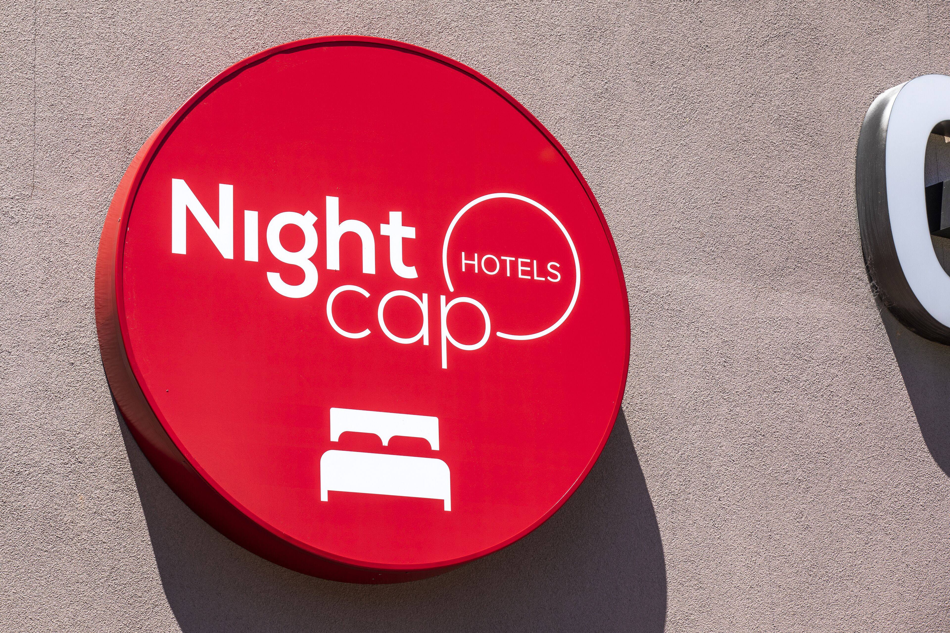 Ein rotes, rundes Schild mit dem Schriftzug "Nightcap Hotels" und einem Bett-Symbol, das ein Hotel oder einen Standort kennzeichnet.