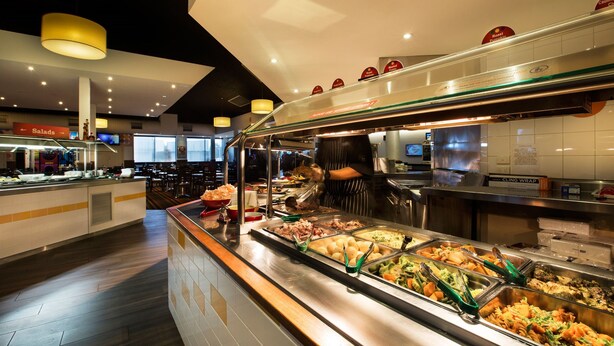 A buffet area with various food options and a person serving food. - Nightcap at Gateway Hotel (Corio)
