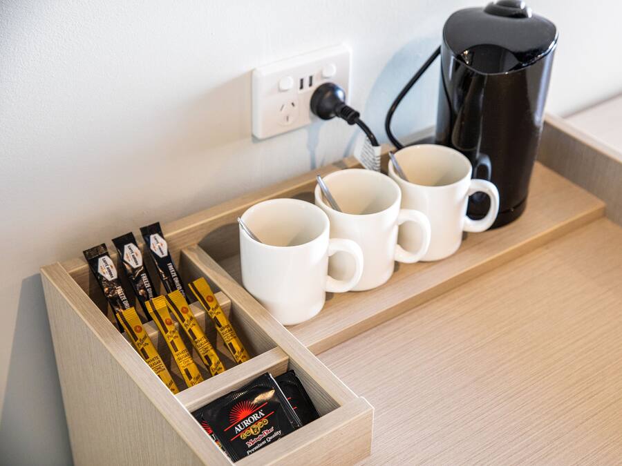A wooden tray with three white mugs and a black coffee maker, connected to a power outlet.