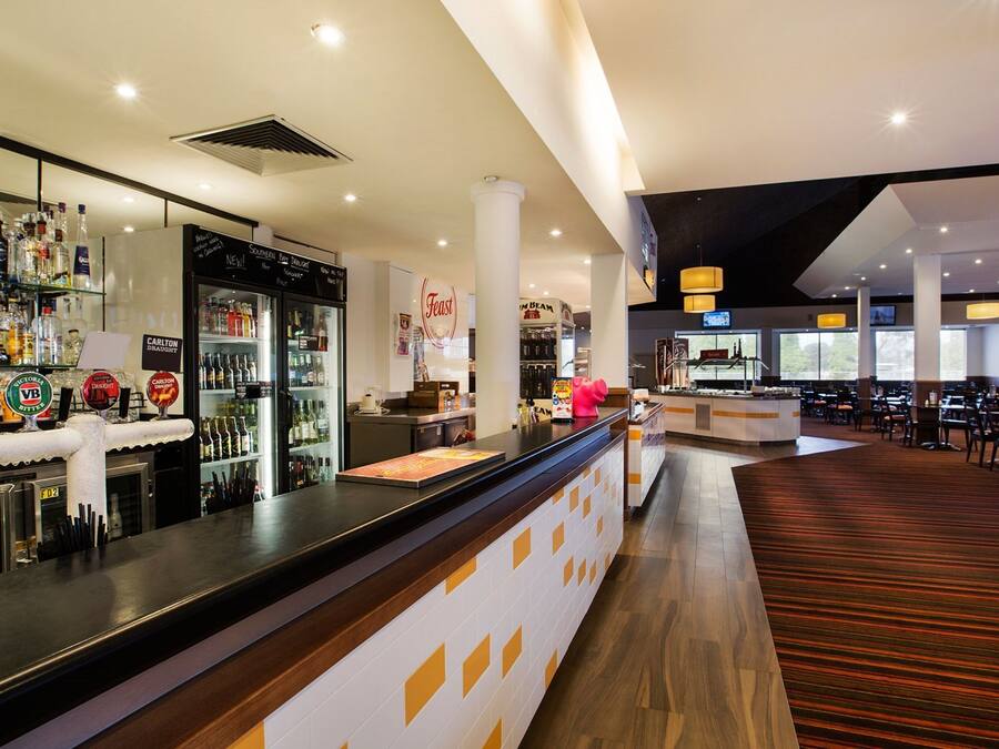 A bar area with a counter, shelves of liquor bottles, a refrigerator, and a seating area with tables and chairs.