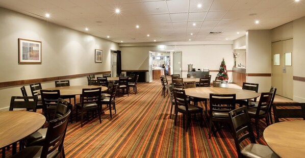 A hotel conference room with multiple tables and chairs, a carpeted floor, and a Christmas tree.