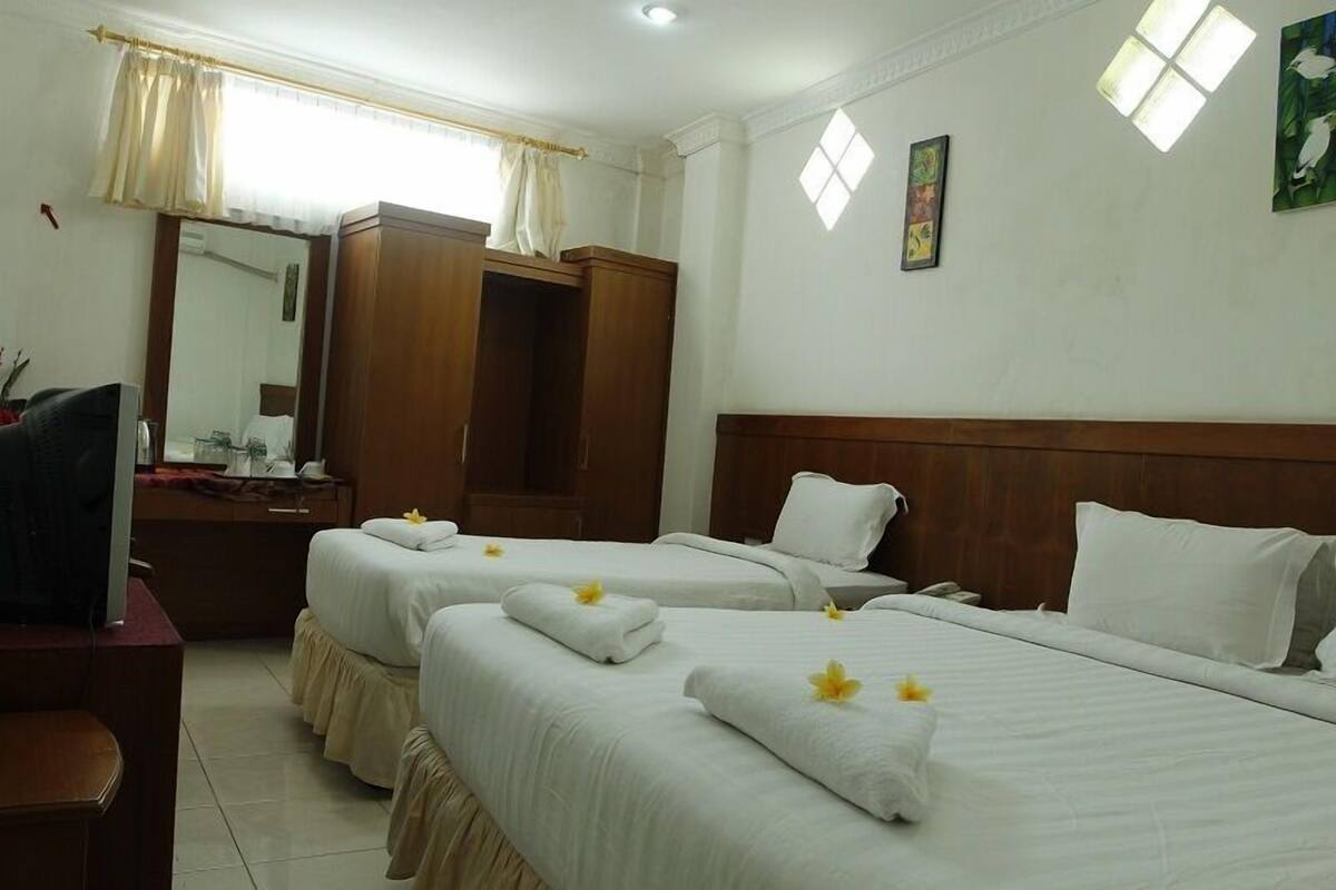 A hotel room with two beds, a wooden wardrobe, a desk with a television, and a window with curtains.