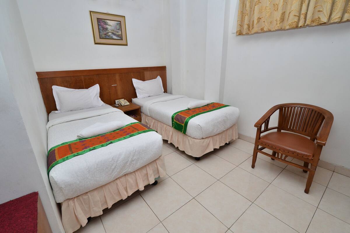 A hotel room with two single beds, a wooden chair, a telephone, and a framed picture on the wall.