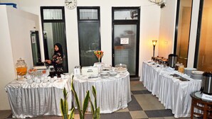 Habitación de hotel con piso a cuadros, un reloj en la pared y una mesa de buffet con diferentes alimentos y una copa decorativa.