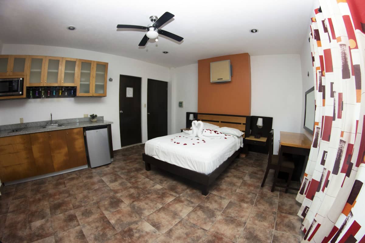 A bedroom with a bed, a desk, a microwave, and a small refrigerator.