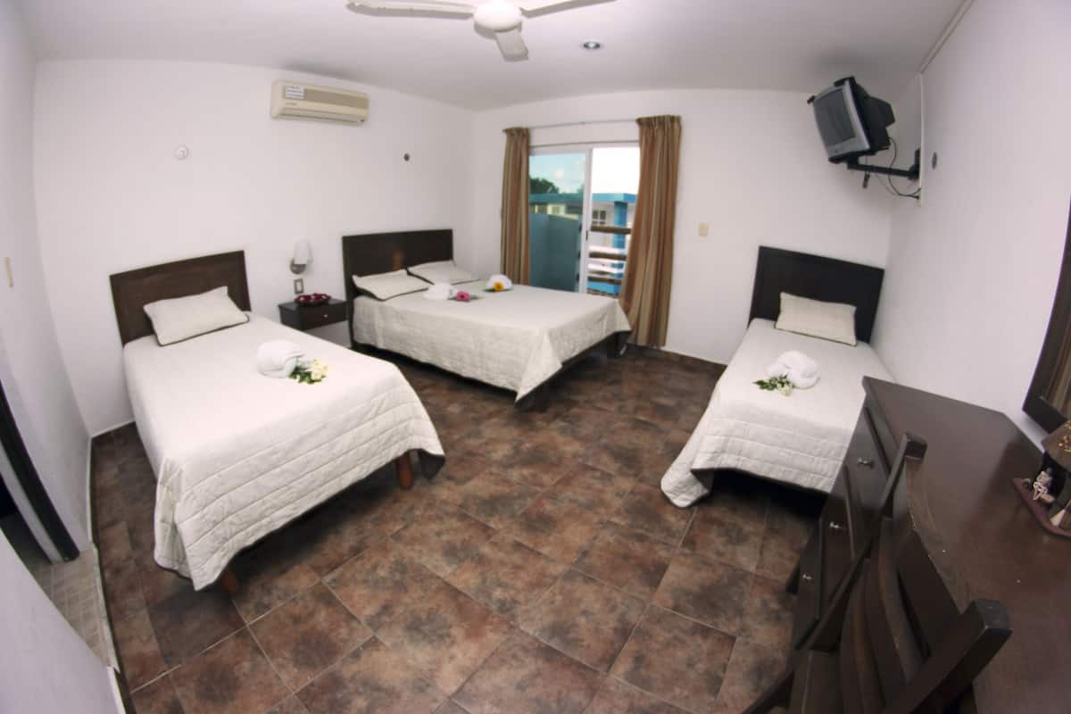 A hotel room with three single beds, a ceiling fan, a television mounted on the wall, and a balcony with a view.