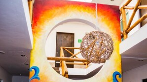 Un mural colorit amb un flamenc, una finestra circular i una llum penjant en un espai interior ampli.