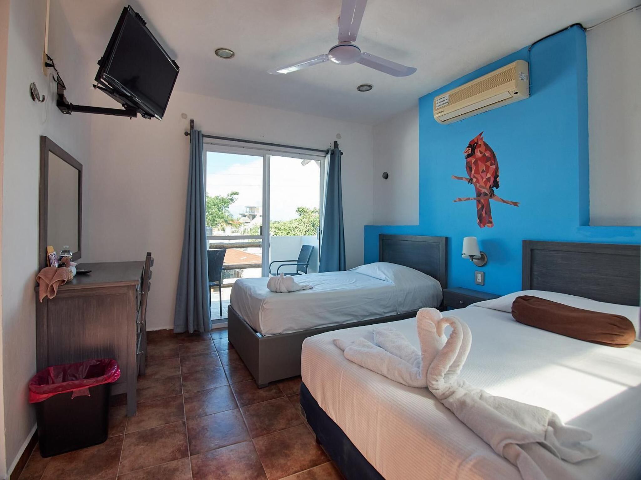 A hotel room with two beds, a desk, a TV, and a balcony with a view.