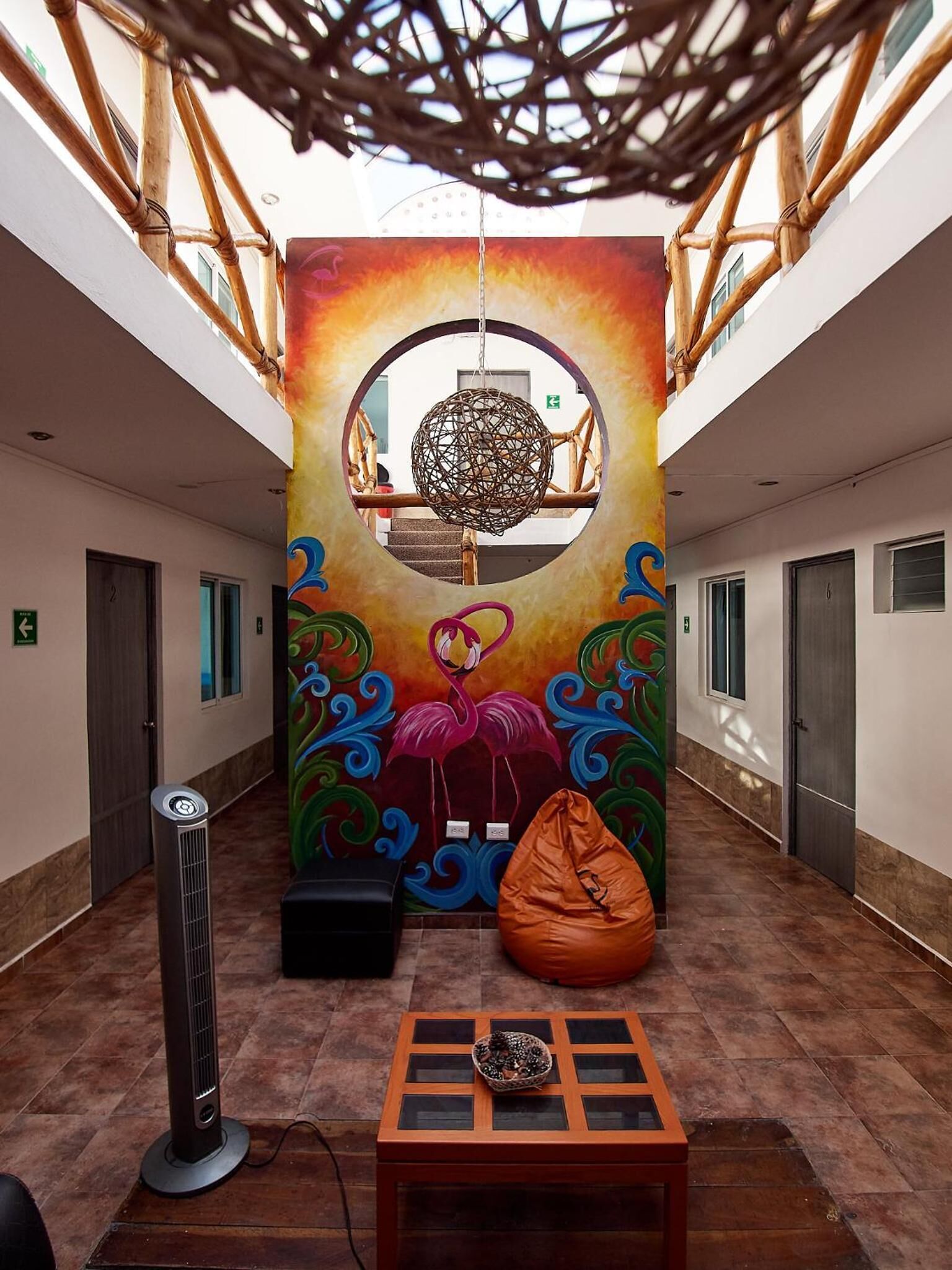 A hallway with a colorful mural of a flamingo, a hanging spherical decoration, and a seating area with a table and bean bag.
