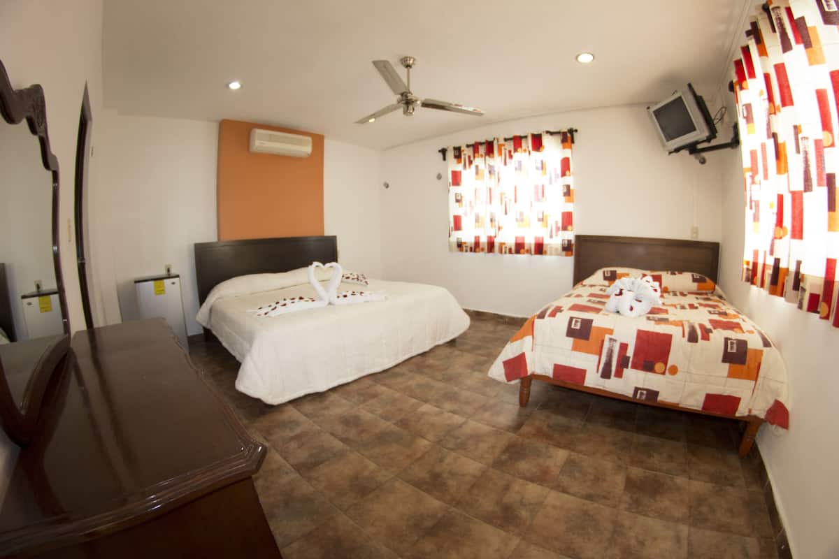 A hotel room with two beds, a desk, a ceiling fan, an air conditioning unit, and a television mounted on the wall.