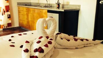 A bed with a towel shaped like a swan, a bottle of wine, and a glass on the nightstand.
