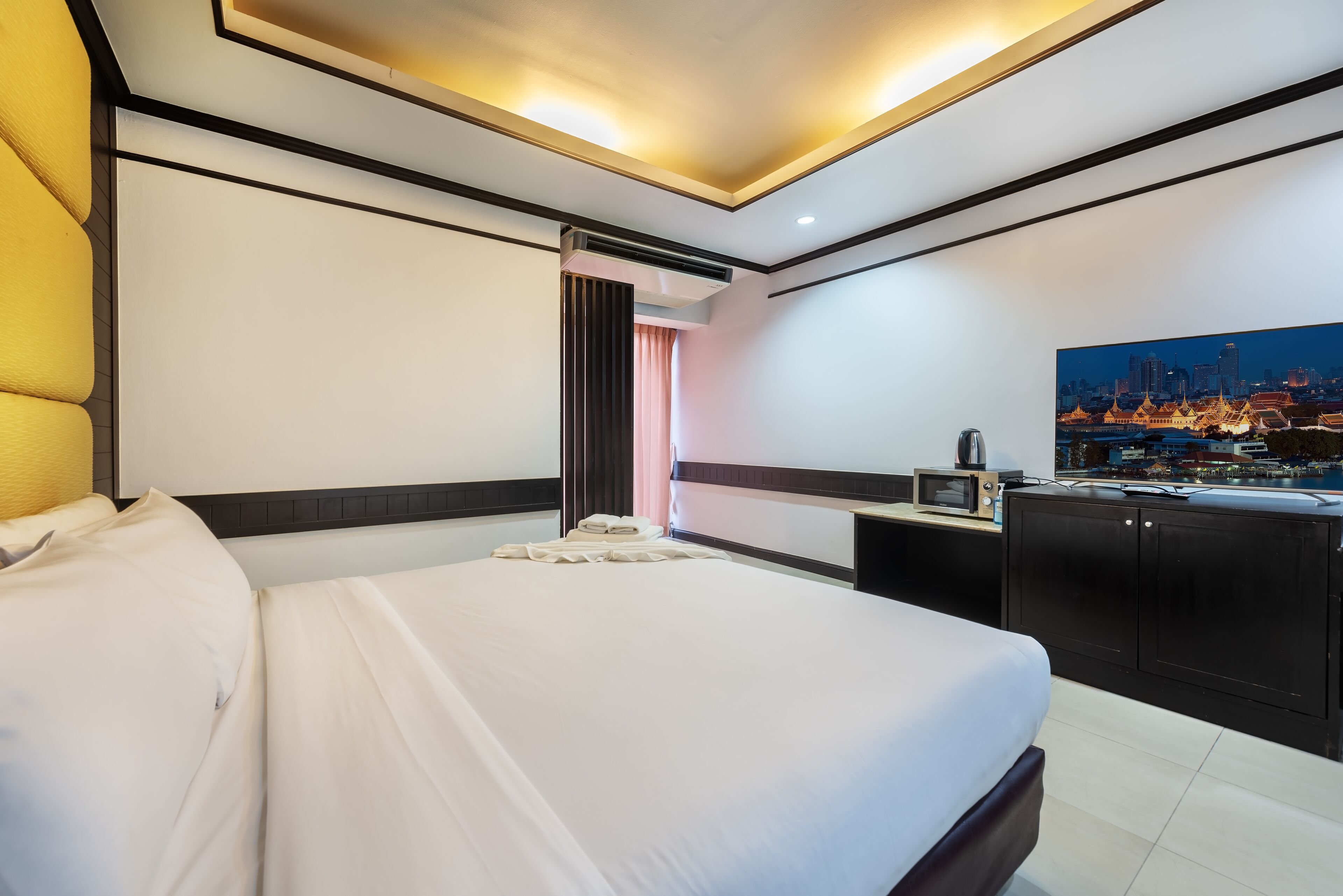 Una habitación de hotel con una cama grande, un escritorio con una computadora, un microondas y un cuadro de paisaje urbano en la pared.