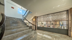 A modern interior with a marble staircase, a glass railing, and a decorative wall with vertical panels. - The Legacy Hotel (Nonthaburi)