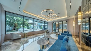 A modern lobby with large windows, a blue sofa, and a unique circular light fixture. - The Legacy Hotel (Nonthaburi)
