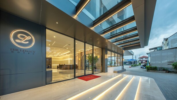The exterior of The Legacy Hotel with a modern design, large glass windows, and a red doormat at the entrance. - The Legacy Hotel (Nonthaburi)