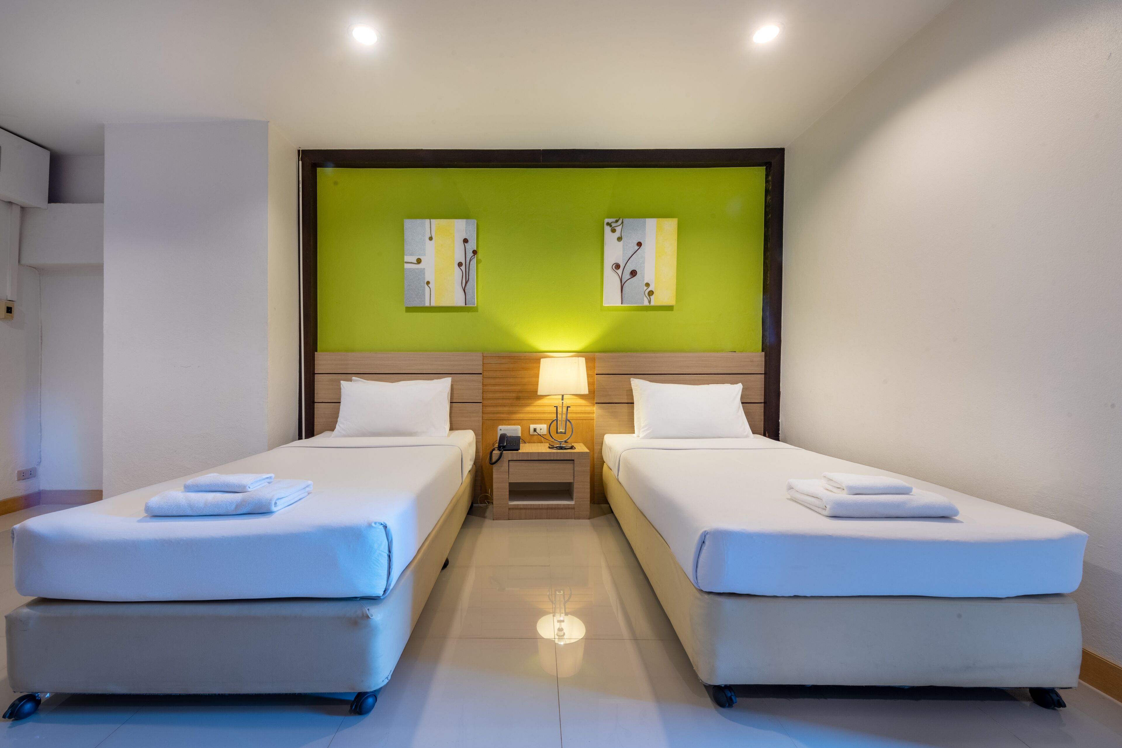 Ein Hotelzimmer mit zwei Betten, einer grünen Akzentwand und Bildern über den Betten.