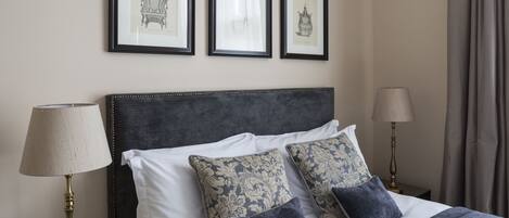 A neatly made bed with a dark headboard, two bedside lamps, and three framed pictures on the wall.