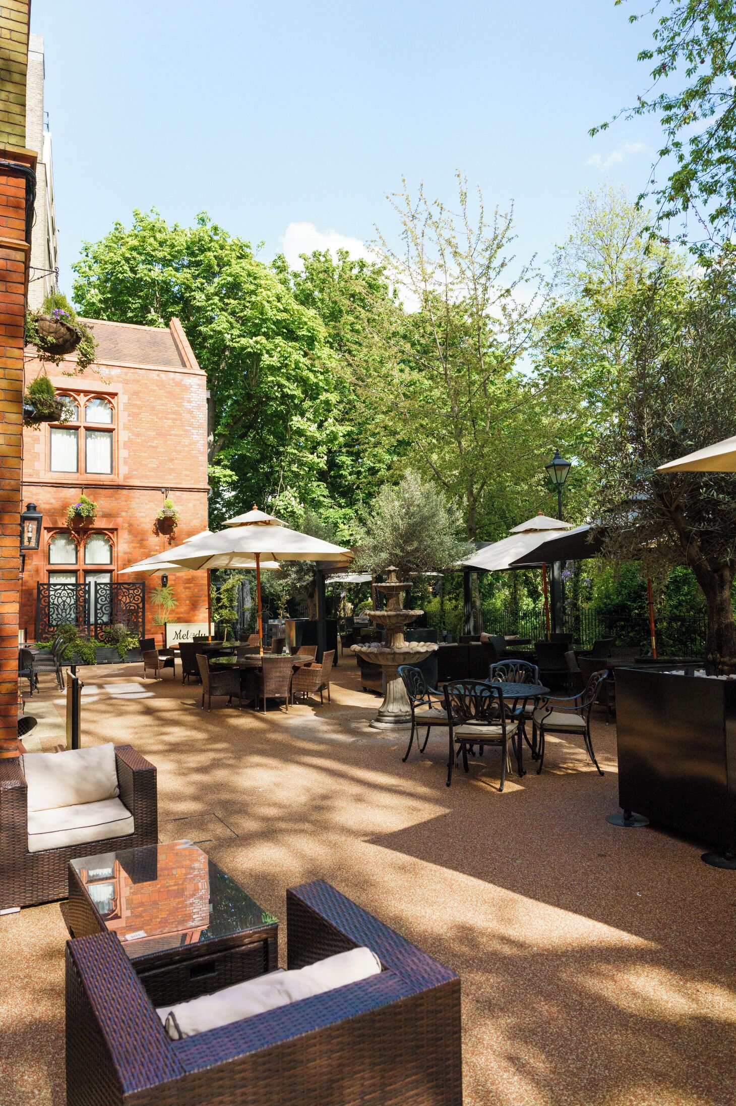 An outdoor patio with wicker furniture, umbrellas, and a brick building in the background.