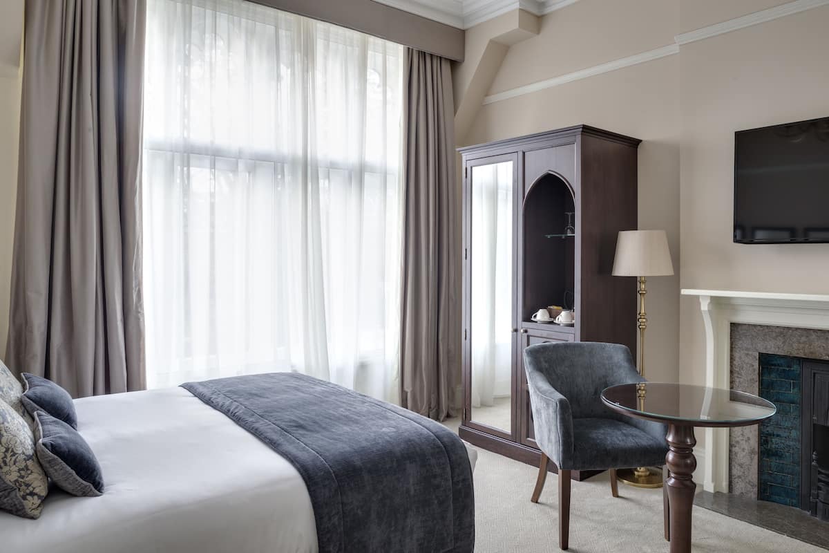 A hotel room with a bed, a chair, a table, a wardrobe, and a fireplace.