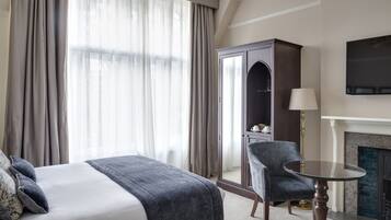 A hotel room with a bed, a chair, a table, a wardrobe, and a fireplace.