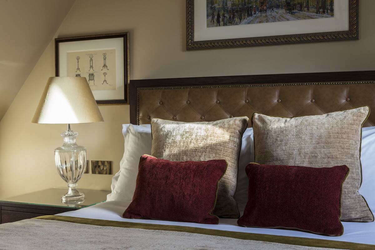 A neatly made bed with a tufted headboard, a bedside lamp, and two framed pictures on the wall.