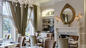 Un coin repas avec des tables dressées pour le repas, une cheminée et un grand miroir au mur.