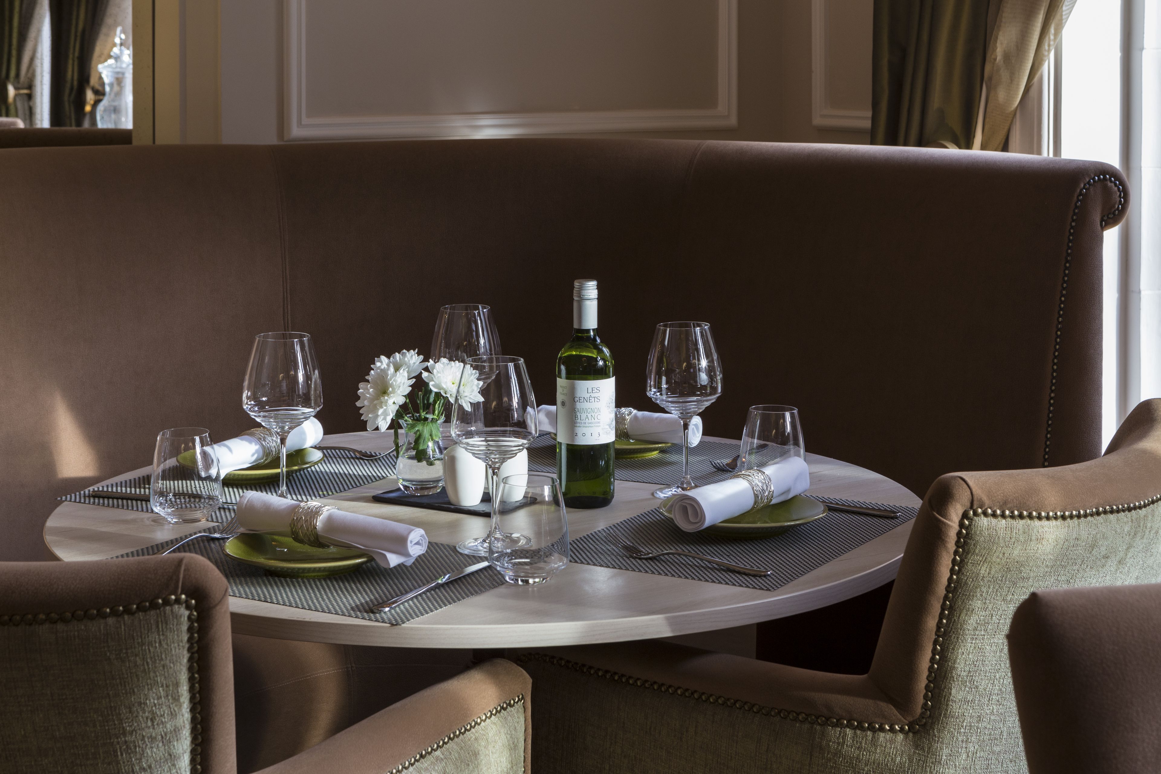 A dining table set with wine glasses, a bottle, and a vase with flowers.