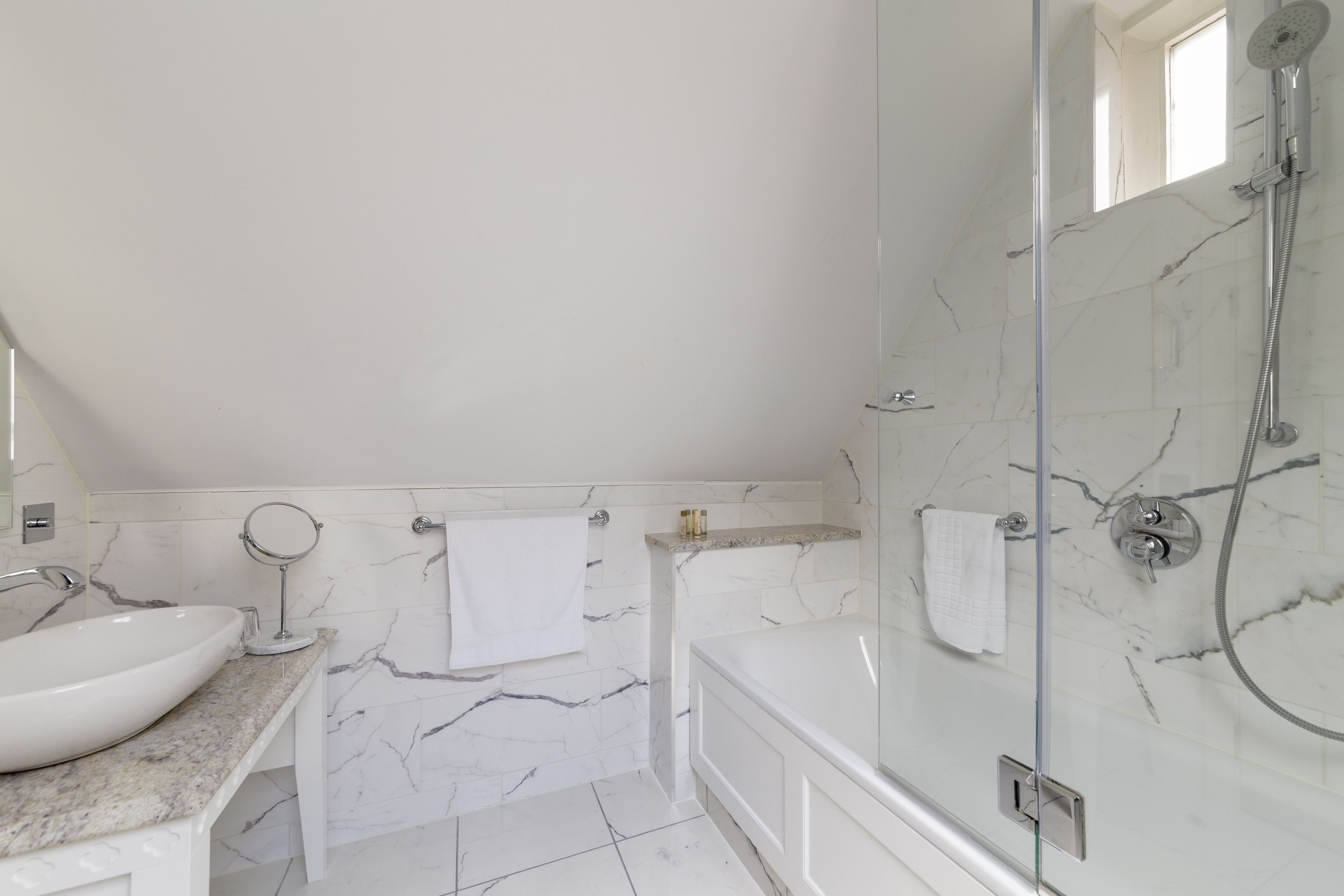 A modern bathroom with a marble sink, a bathtub, and a glass-enclosed shower area.