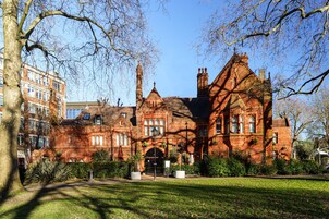 A large red brick building with a prominent entrance, surrounded by a well-maintained lawn and trees.