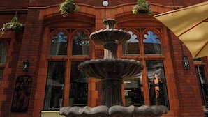 Un bâtiment en briques doté d’une grande fenêtre en arc de cercle et d’une fontaine en pierre devant l’entrée.