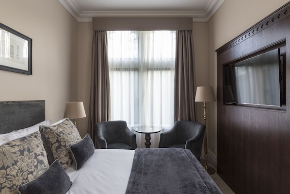 Una habitación de hotel con una cama, dos sillones, una mesita y un televisor.