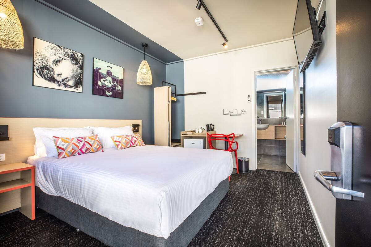 Una habitación de hotel moderna con una cama grande, un escritorio, una silla y un baño visible a través de una puerta abierta.