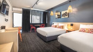 A hotel room with two beds, a desk, a chair, and a TV on the wall.