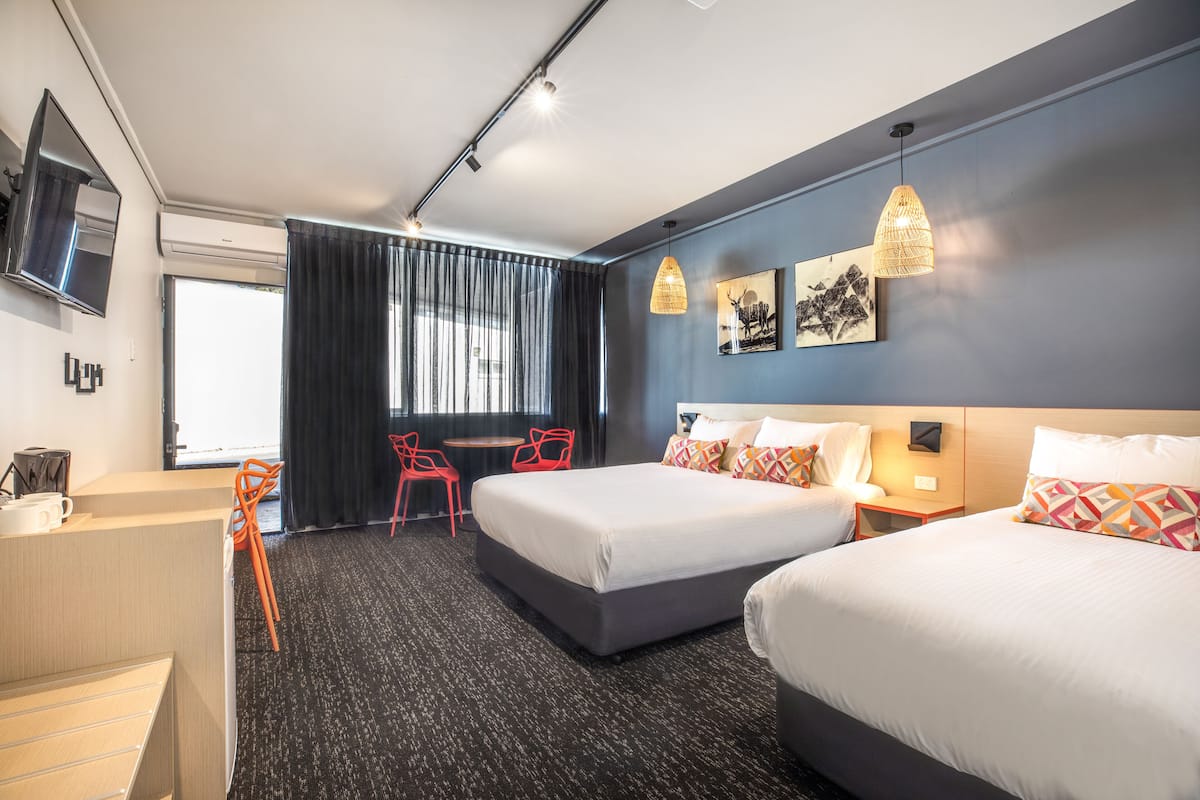 Habitación de hotel con dos camas, un escritorio, una silla y un televisor en la pared.