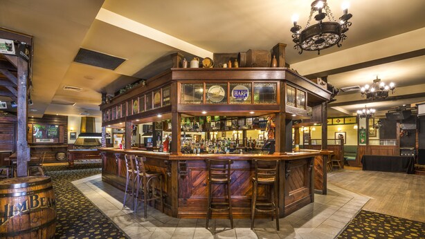 A bar with a double-height structure, wooden bar stools, and a patterned carpet.