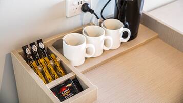 Una bandeja de madera con tres tazas blancas y una cafetera negra conectada a un enchufe.