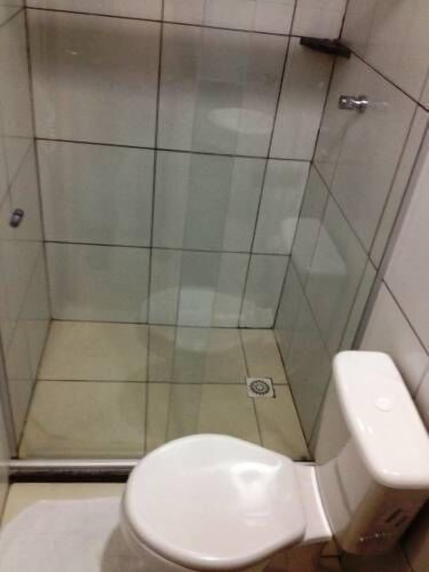Un box de ducha pequeño y cerrado con puerta de cristal, un inodoro blanco y un desagüe visible.
