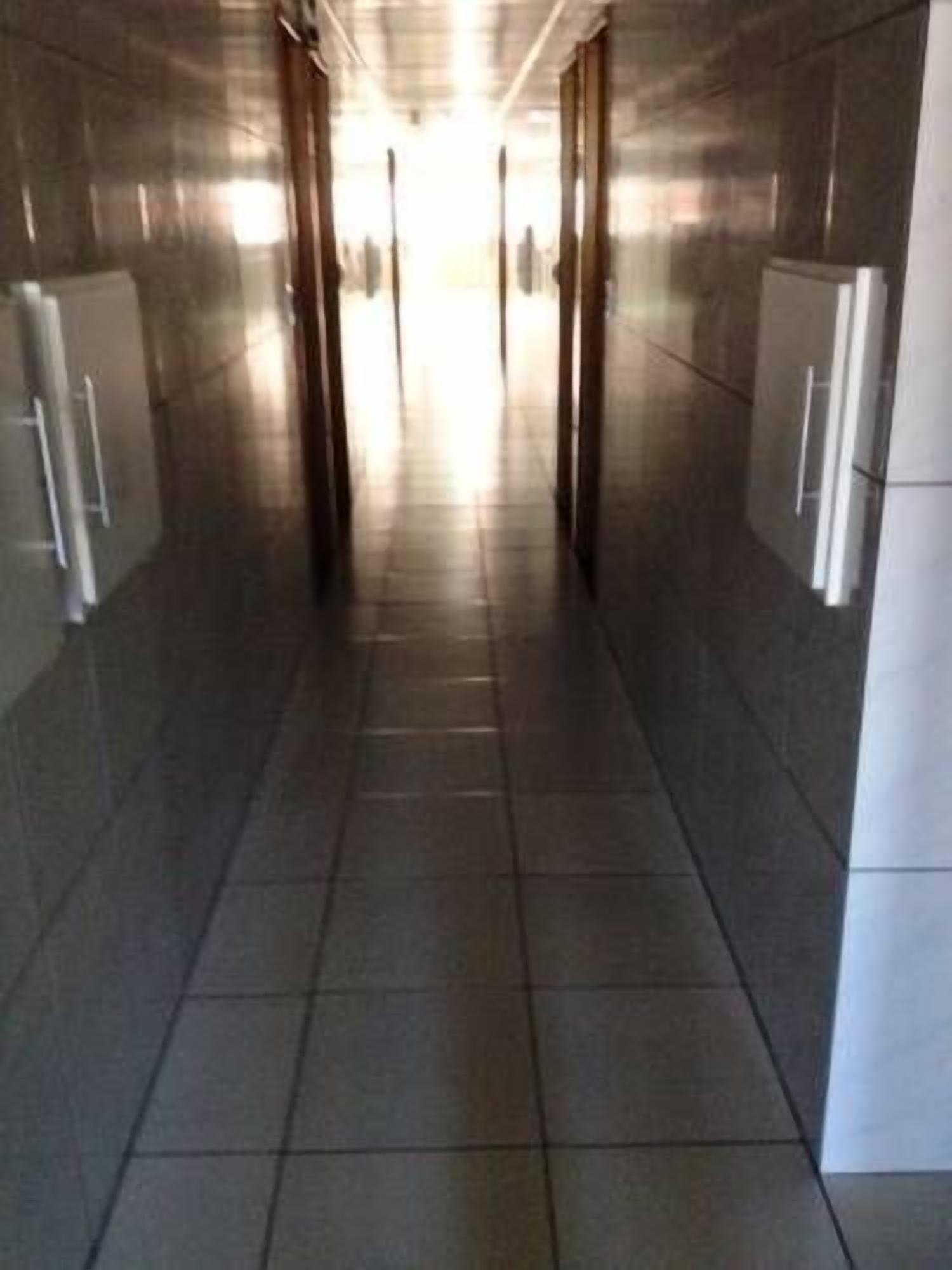Um corredor com paredes e chão revestidos de azulejos, que leva a uma área iluminada no final.