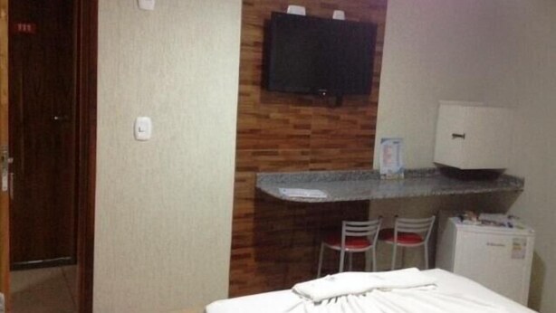 A hotel room with a bed, a small desk with a chair, a television mounted on the wall, and a refrigerator. - Hotel Atlanta (Salvador)