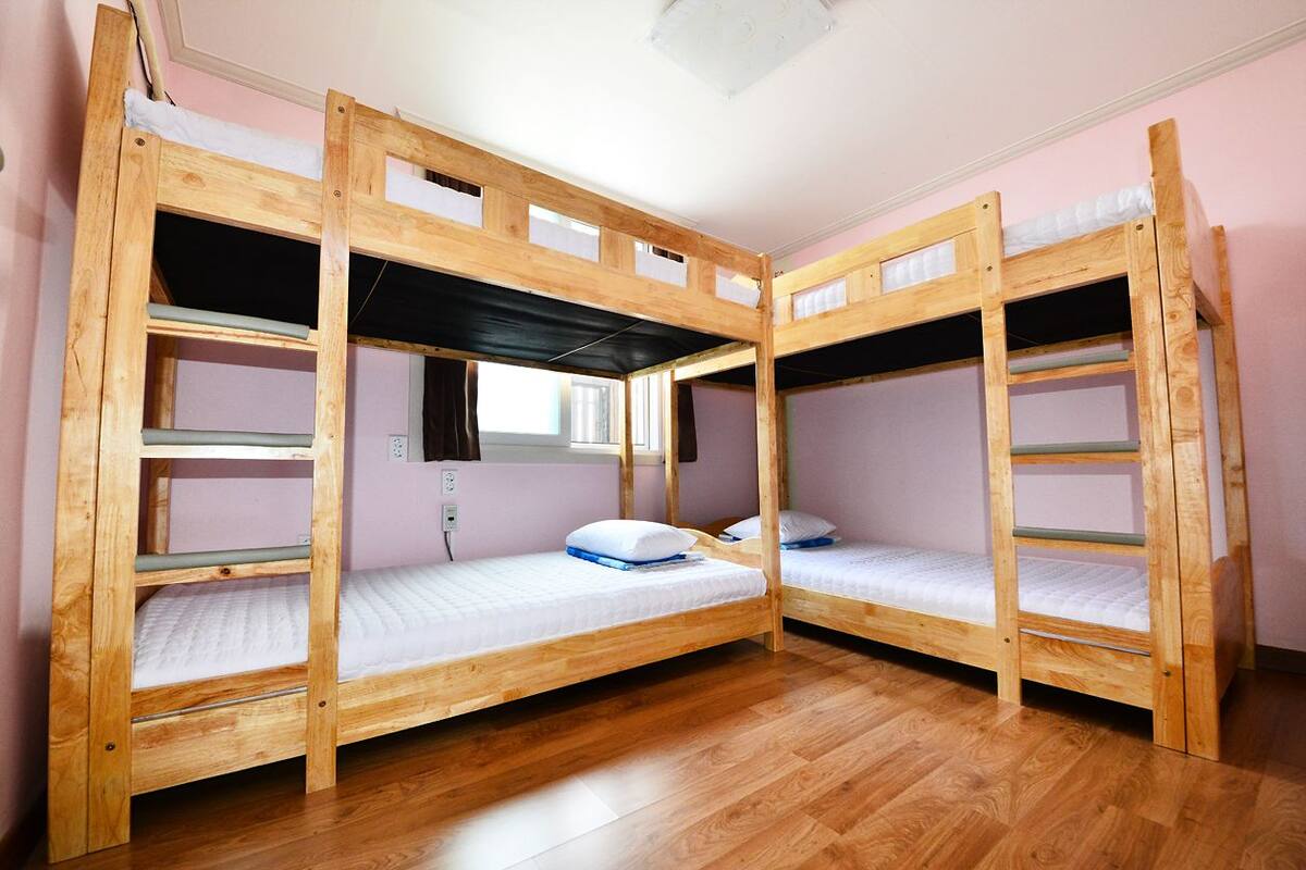 A bunk bed room with wooden frames, a window, and a power outlet.