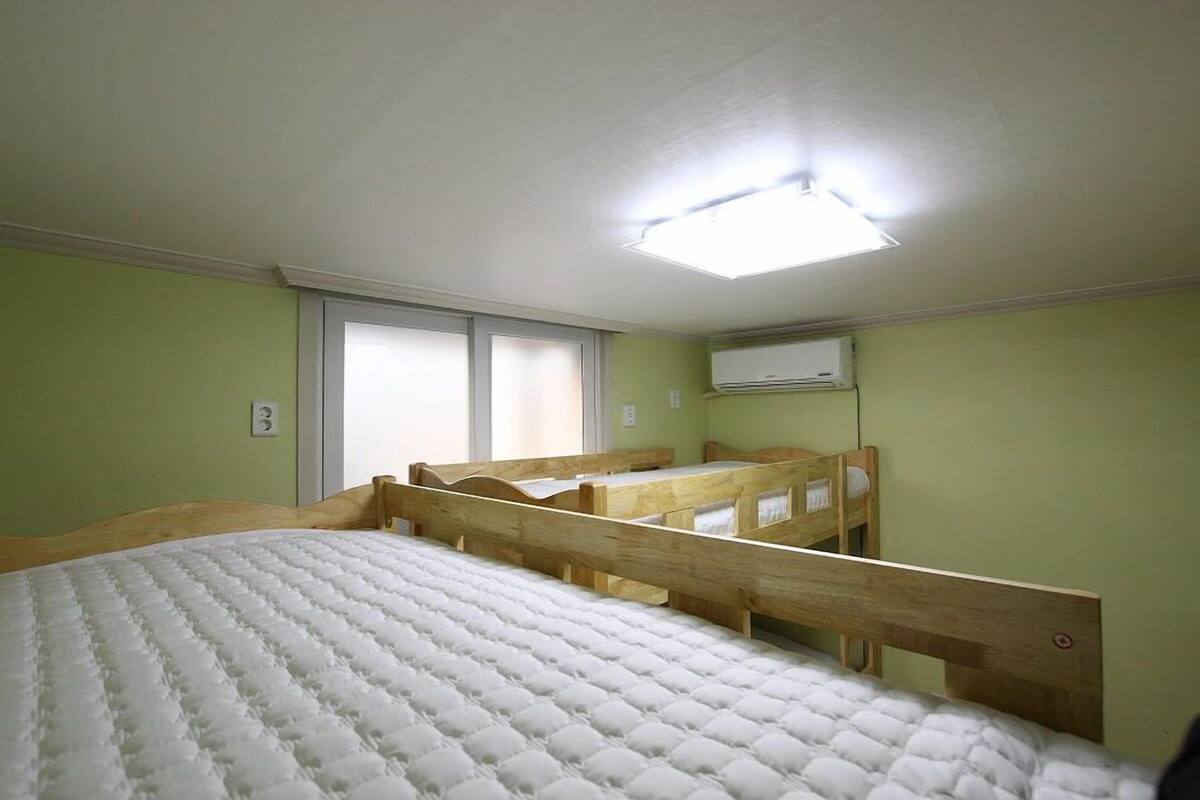A room with a large bed, a wooden bunk bed, and a ceiling light.