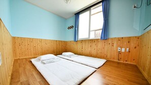 Ein Zimmer mit Holzwänden und Holzböden, zwei Betten, einem Fenster mit blauen Vorhängen und einer Deckenleuchte.