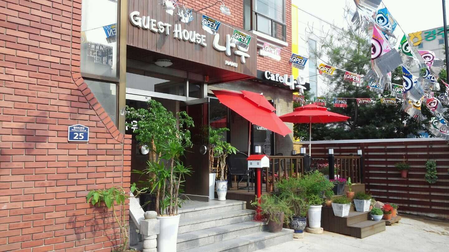 A brick building with a sign reading "Guest House" and "Cafe". There are potted plants and red umbrellas outside.