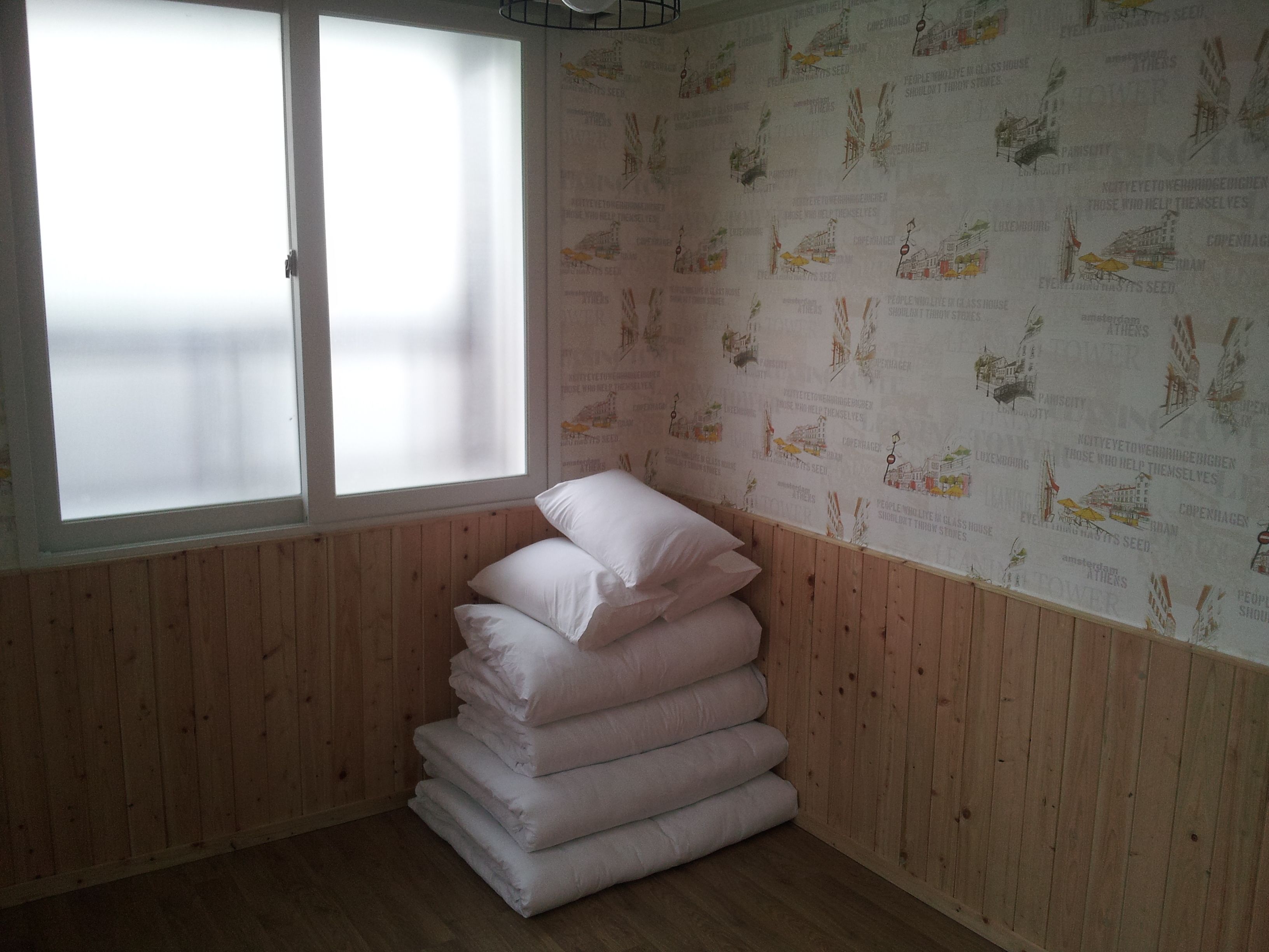 A room with a wooden paneled wall, a window with frosted glass, and a wall with printed illustrations of cities.
