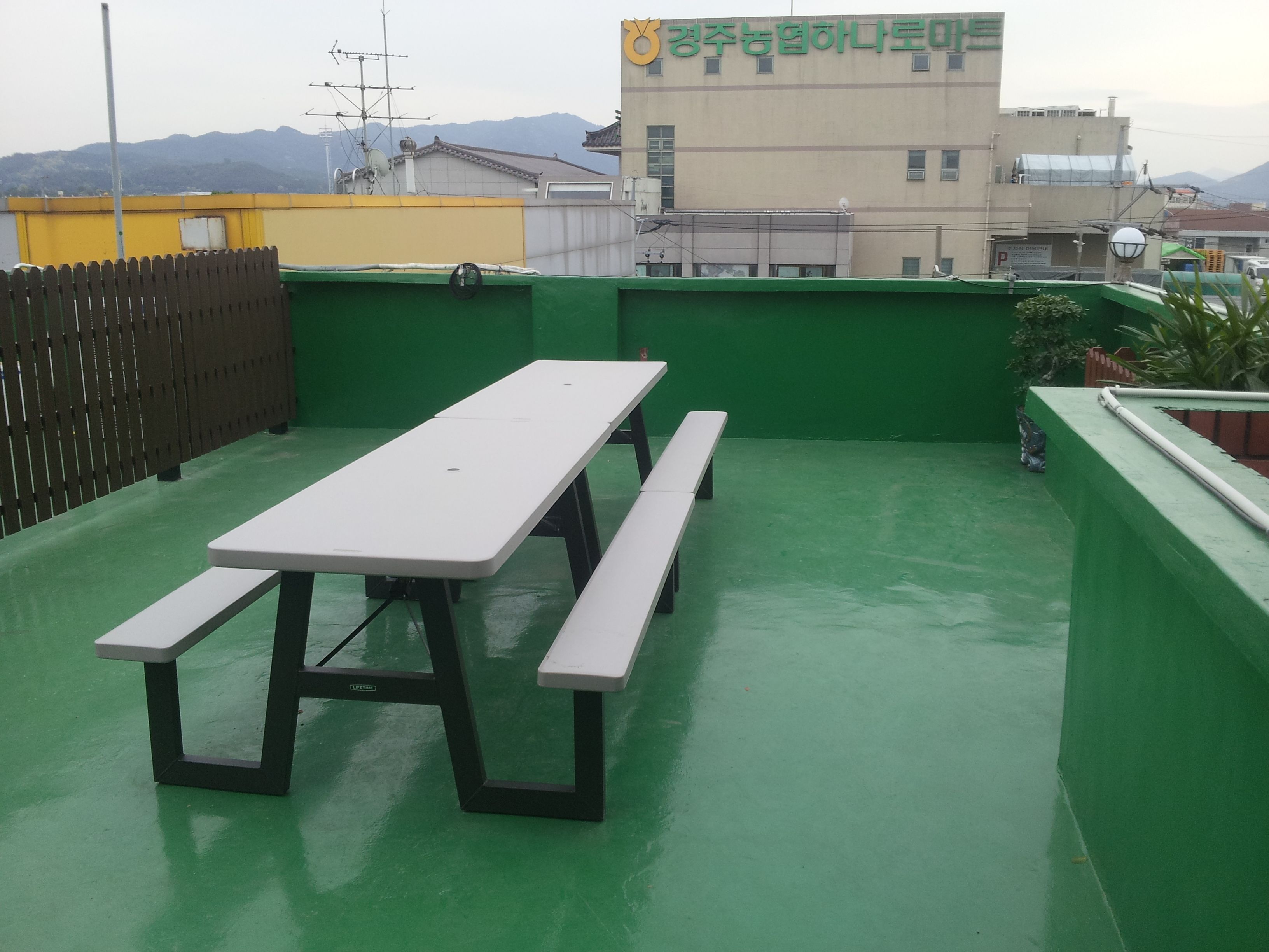Eine Dachterrasse mit Picknicktisch und Bänken, umgeben von grünen Wänden und einem gelben Zaun.