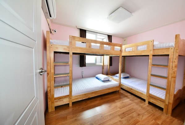A room with three bunk beds, wooden flooring, a window with curtains, and a door.