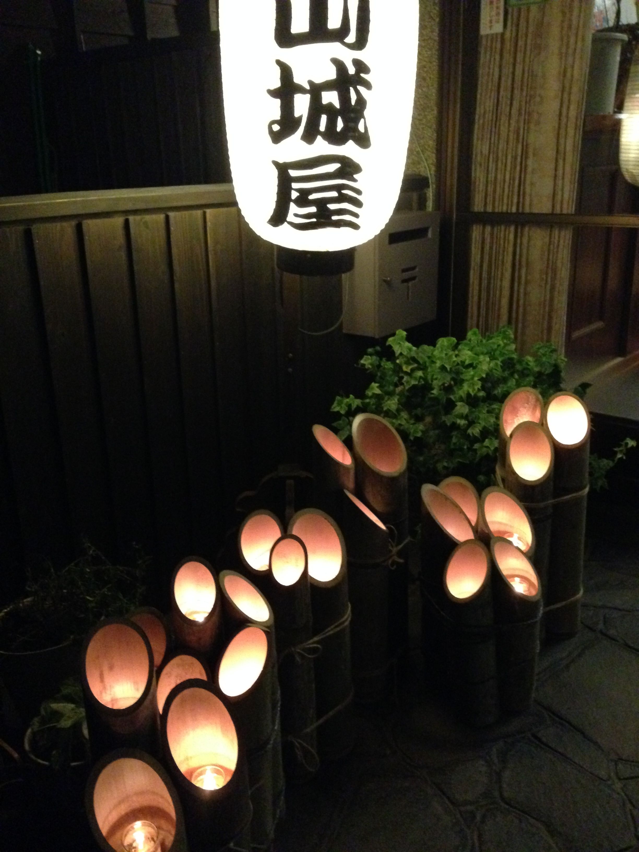 A row of illuminated cylindrical lanterns, a wooden fence, and a sign with Japanese characters.