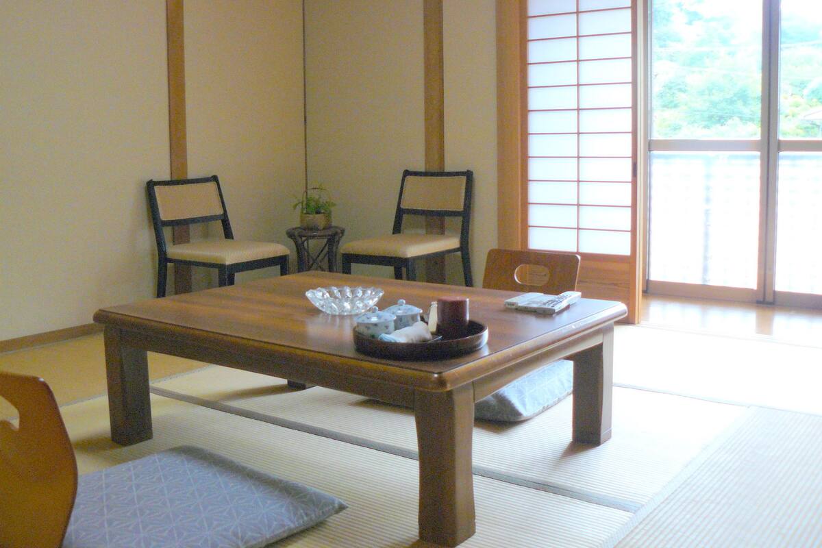 A traditional Japanese room with tatami flooring, a low wooden table, and two chairs.