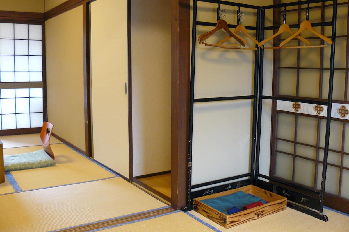 A traditional Japanese room with tatami flooring, sliding doors, and a wooden shelf with hangers.